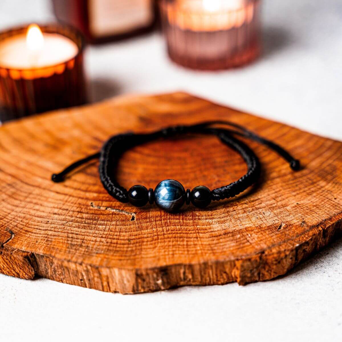 Bracelet with beads on a wooden surface with candles in the background. The Tiger’s Eye Stability Bracelet: Falcon's Eye (Blue Tiger's Eye) with Black Agate