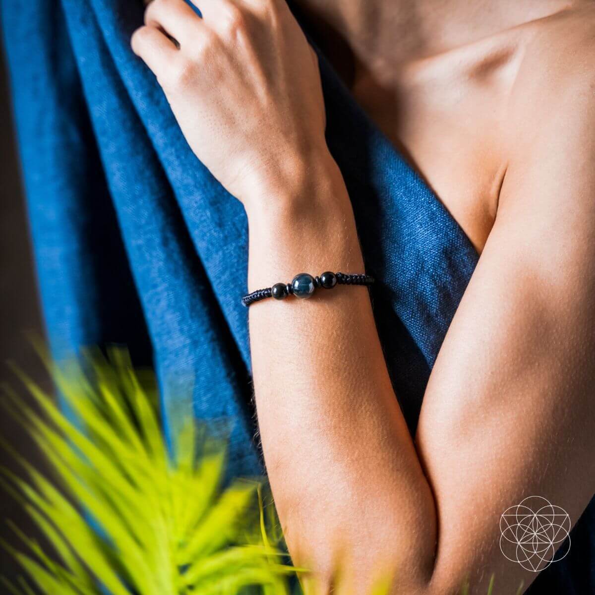 Person wearing a black beaded bracelet with a blue towel and green plant in the background. The Tiger’s Eye Stability Bracelet: Falcon's Eye (Blue Tiger's Eye) with Black Agate