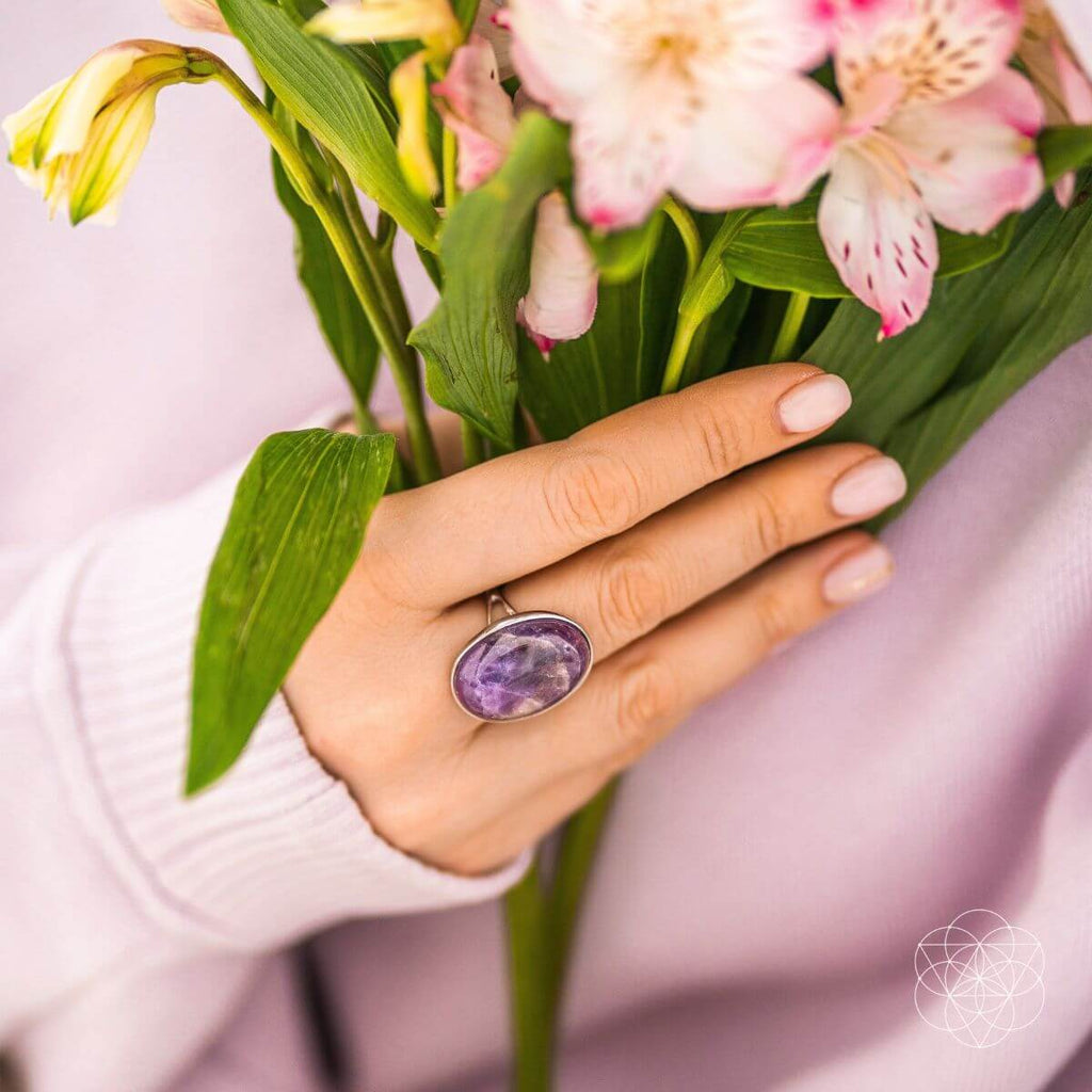 Hand wearing a purple gemstone ring holding a bouquet of flowers. The Visualization Ring: Brass, Platinum and Amethyst