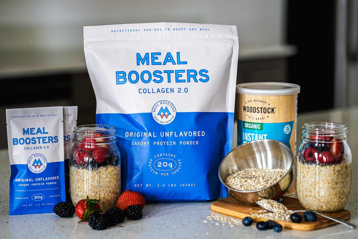 Meal Boosters Original Unflavored Grass-Fed Collagen protein powder in blue and white resealable pouches displayed with overnight oats, fresh berries, rolled oats, and organic instant oats on a kitchen countertop.