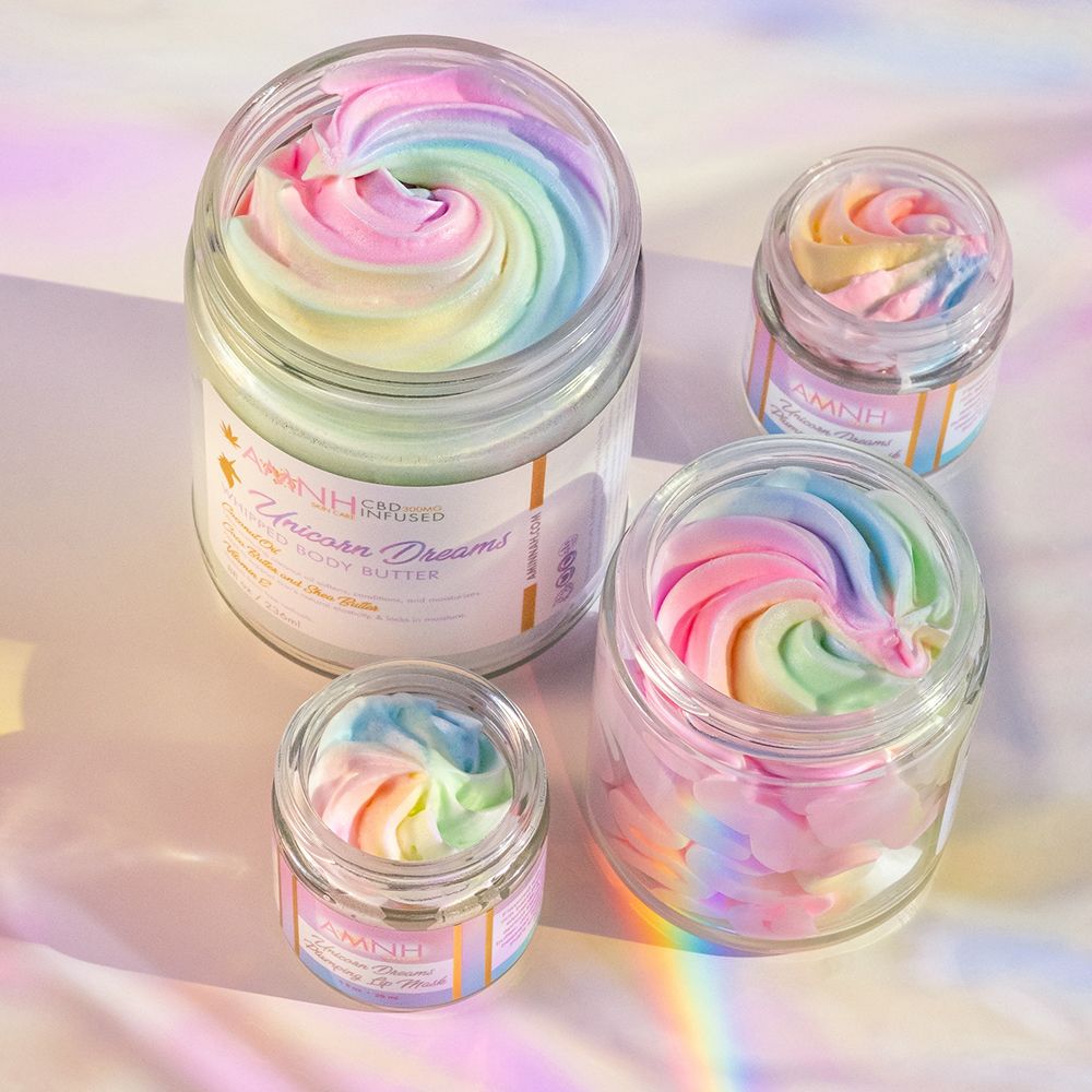 Unicorn Dreams Whipped Body Butter collection featuring pastel rainbow whipped body butter in multiple glass jars. Clean beauty, cruelty-free, vegan, female-owned brand made with natural ingredients including shea butter, cocoa butter, mango butter, coconut oil, jojoba oil, and vitamin E to deeply moisturize, soften, nourish, and protect dry skin with a sweet cotton candy fragrance.