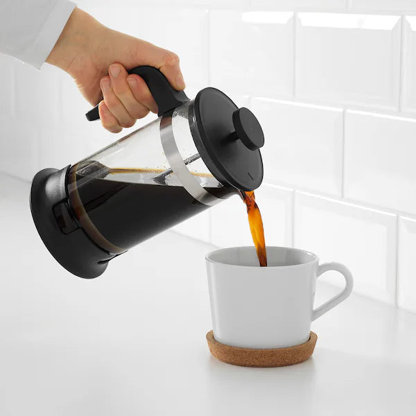 Person pouring rich coffee from a heat-resistant glass French press with stainless steel filter into a white mug, home coffee brewing accessory