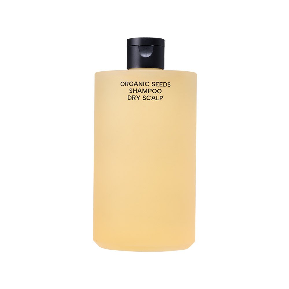 A translucent pale yellow bottle of Whamisa Organic Seeds Shampoo for Dry Scalp, featuring a black cap, centered against a clean, plain white background.
